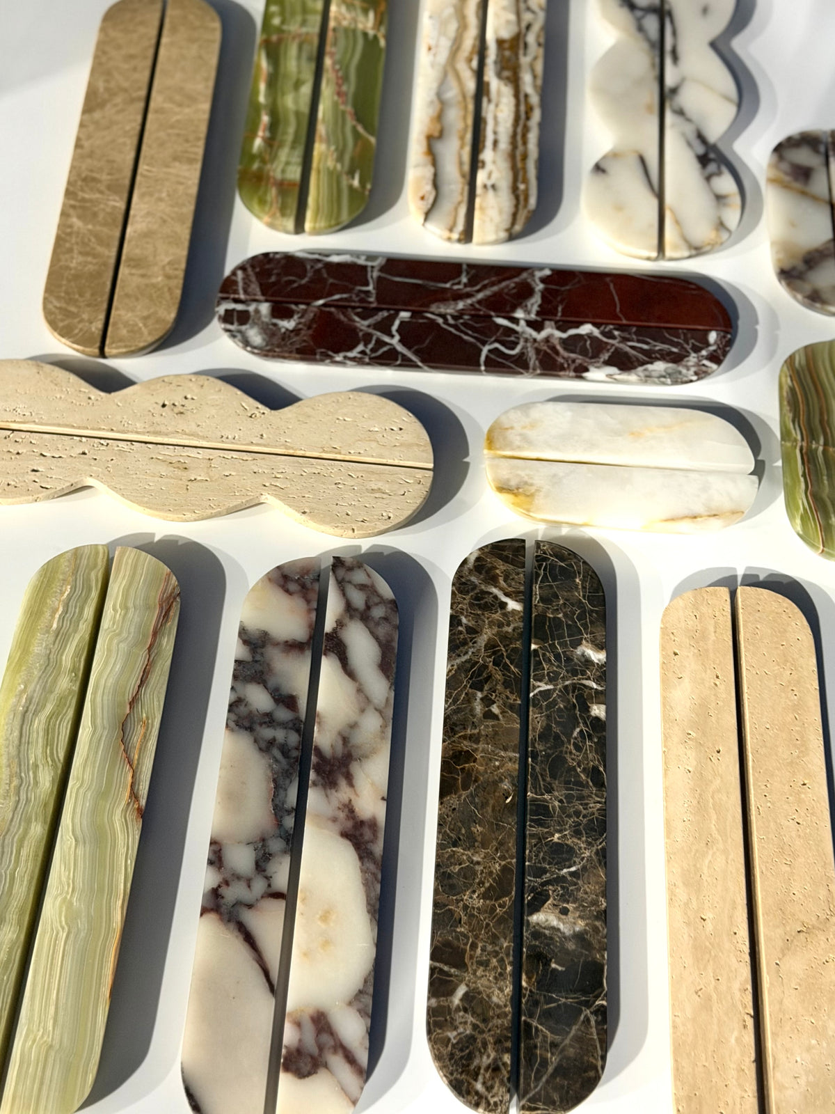 A collection of polished stone elongated bar clasp connectors in various natural marble and granite patterns, arranged on a white background.