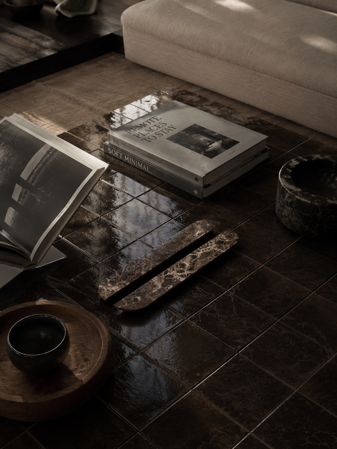 Dark brown glossy ceramic floor tiles styled in a modern interior setting with a beige sofa, books, and wooden accents.