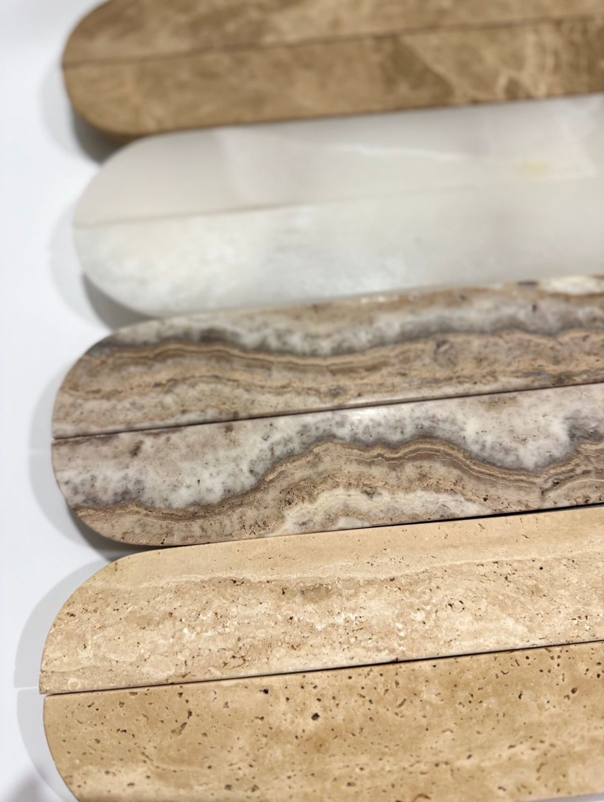 Four polished stone slabs in different natural patterns and colors, arranged vertically on a white background. The stones show variations from light beige and cream to brown, gray, and white marbled textures.