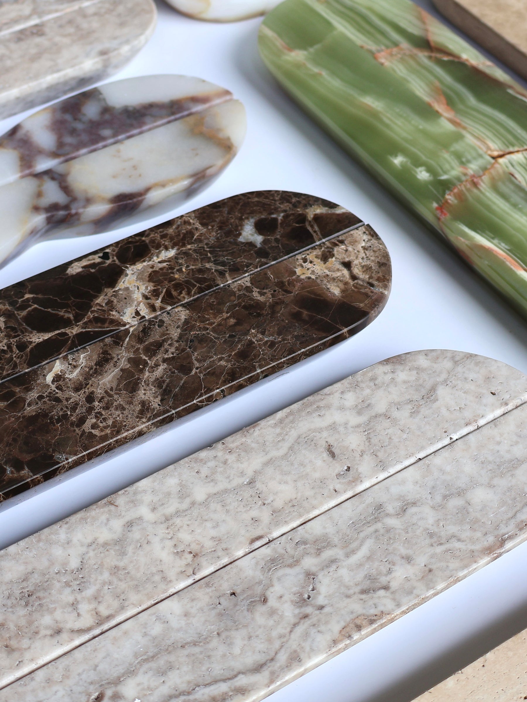 Several polished stone or marble-look pieces arranged diagonally on a white surface, showing varied natural patterns in cream, brown, green, and marbled tones.