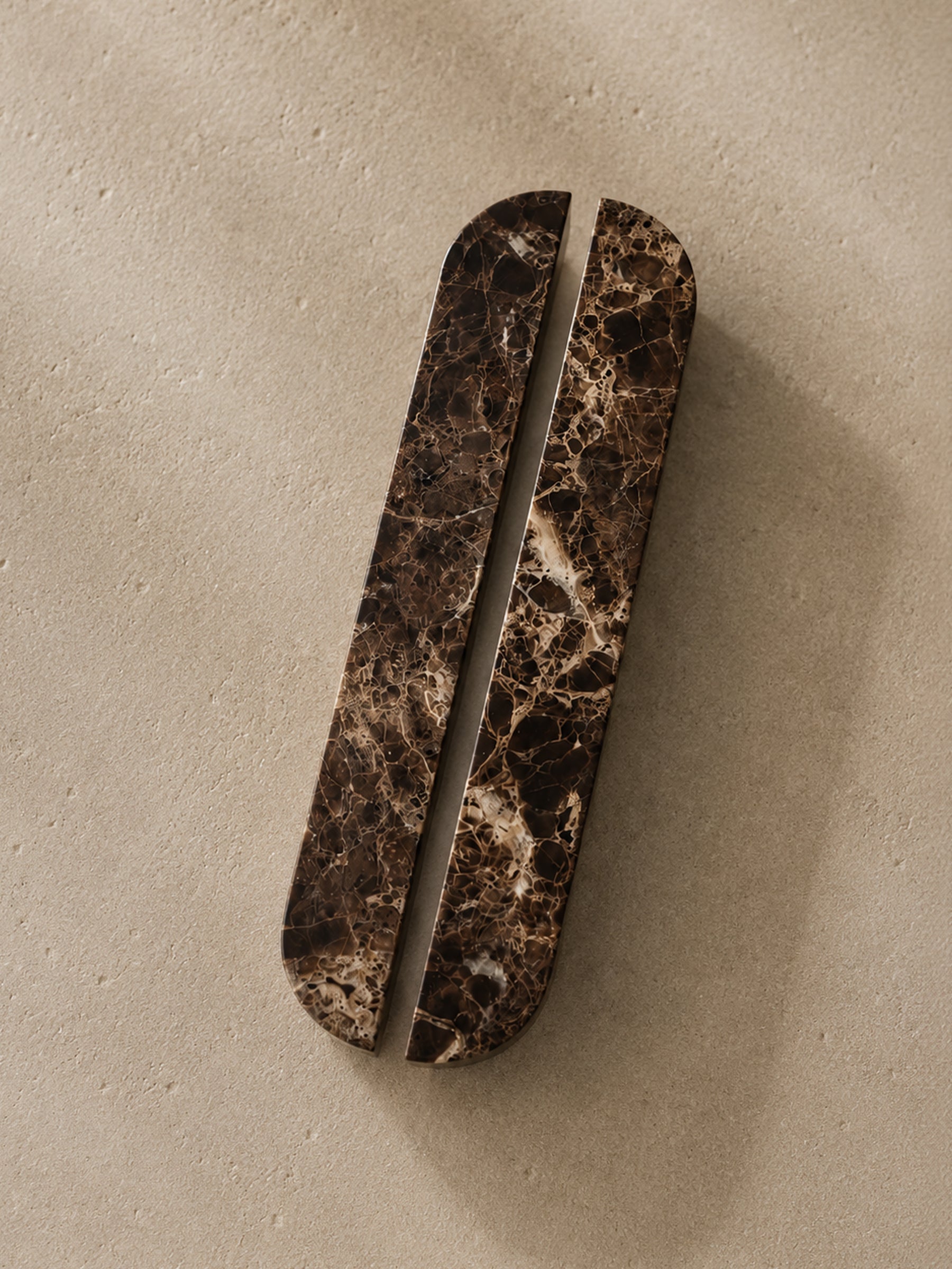 A long, narrow oval cabinet pull handle with a dark brown and black marble pattern, shown on a textured beige background.
