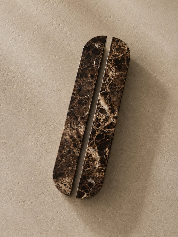 A long, narrow oval cabinet pull handle with a dark brown and black marble pattern, shown on a textured beige background.