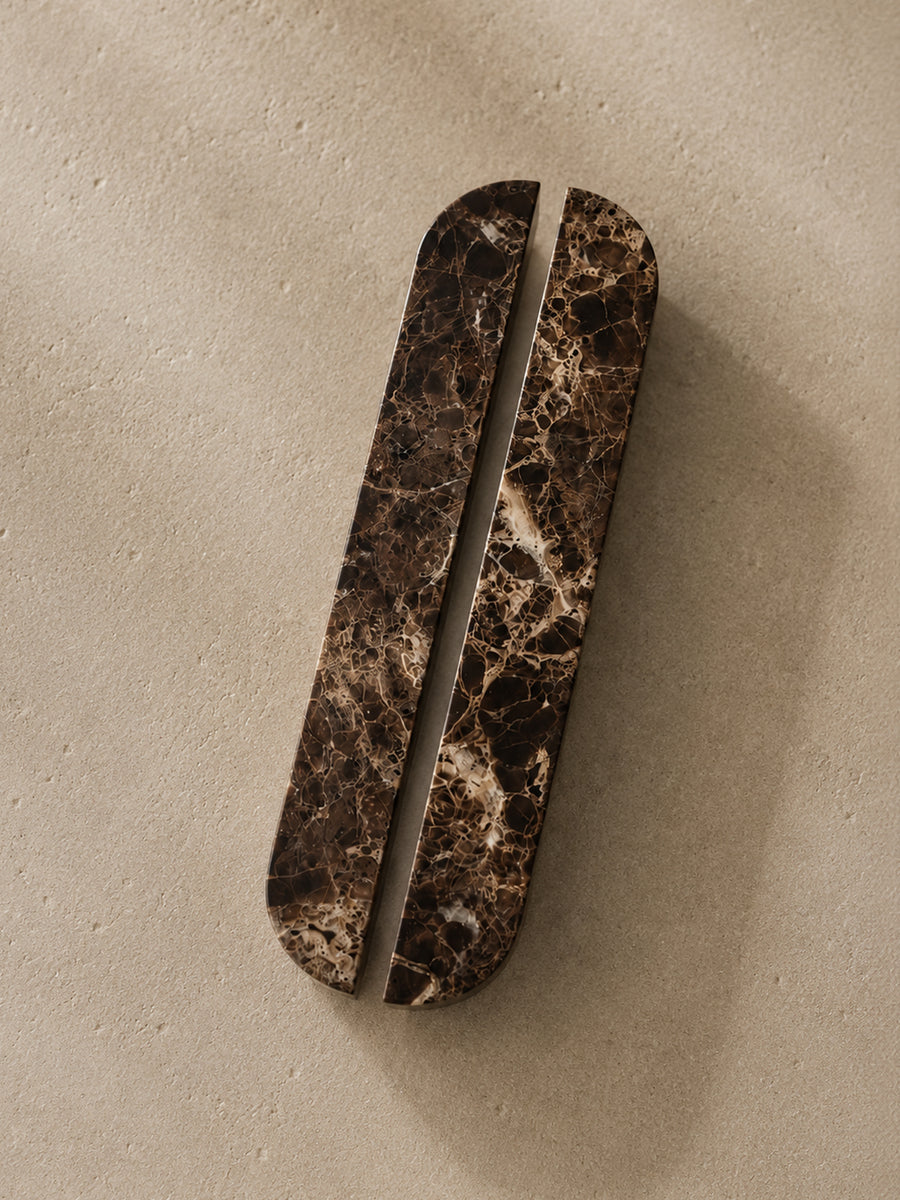 A long, narrow oval cabinet pull handle with a dark brown and black marble pattern, shown on a textured beige background.