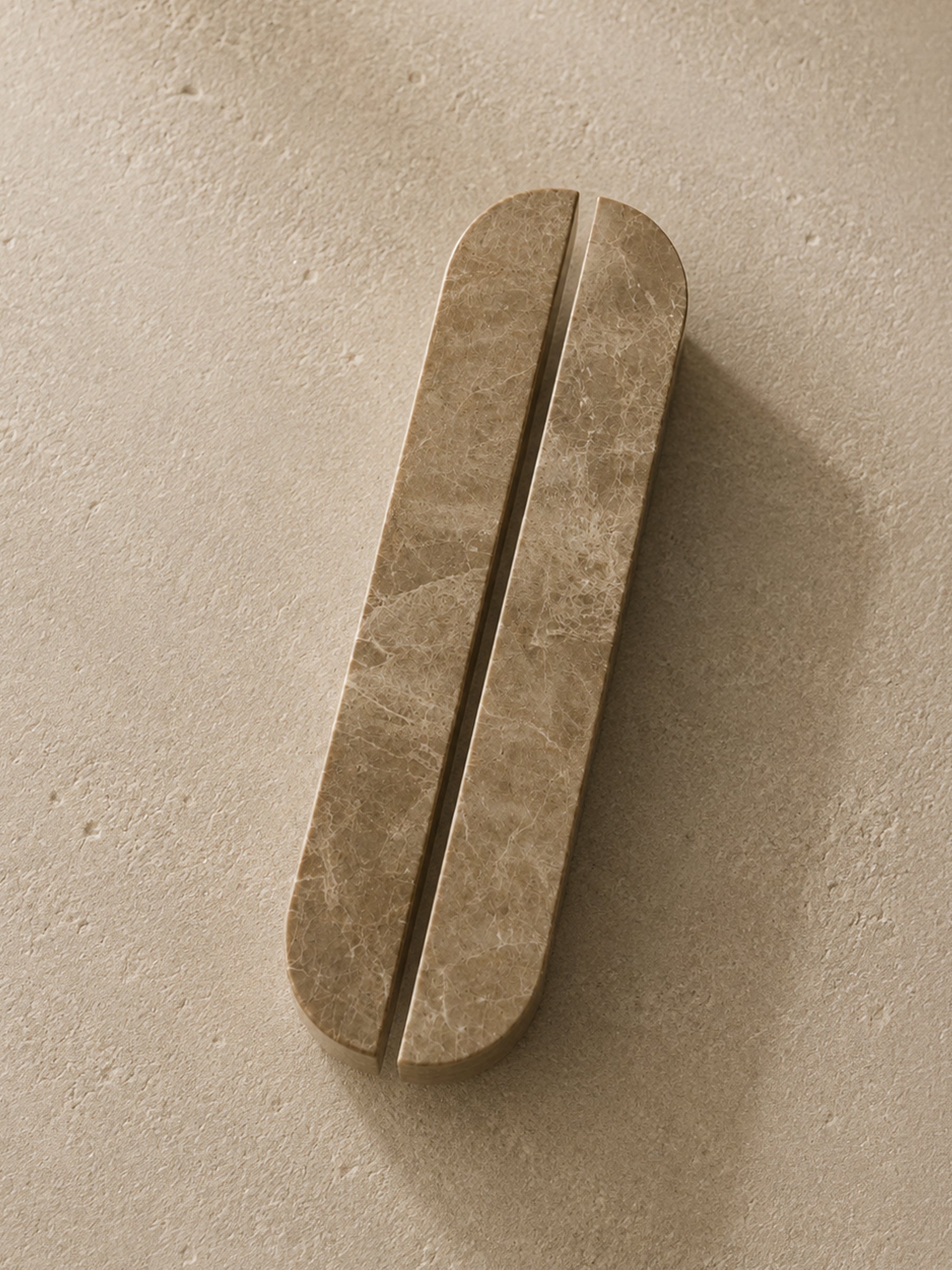 A pair of elongated, rounded bar handles with a warm beige marble texture, shown on a matching textured beige background.