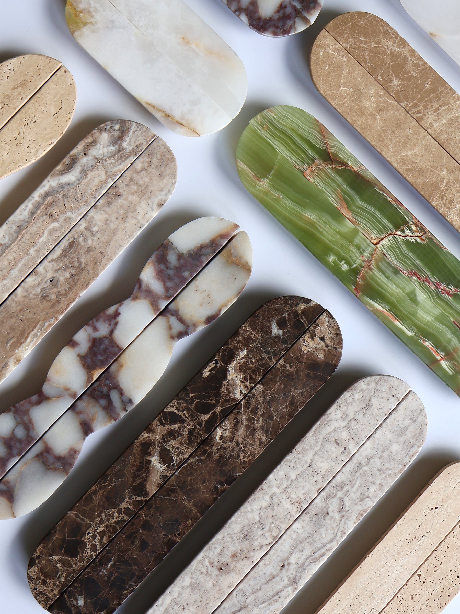 A flat-lay arrangement of elongated stone-look tiles in various natural marble and granite patterns, including beige, brown, green, and cream, on a white background.