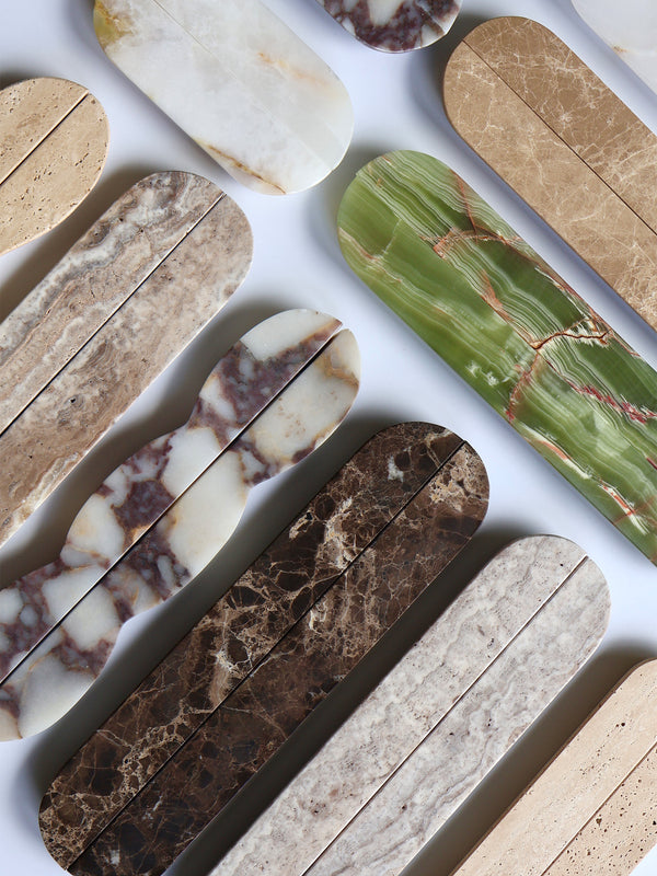 A flat-lay arrangement of elongated stone-look tiles in various natural marble and granite patterns, including beige, brown, green, and cream, on a white background.