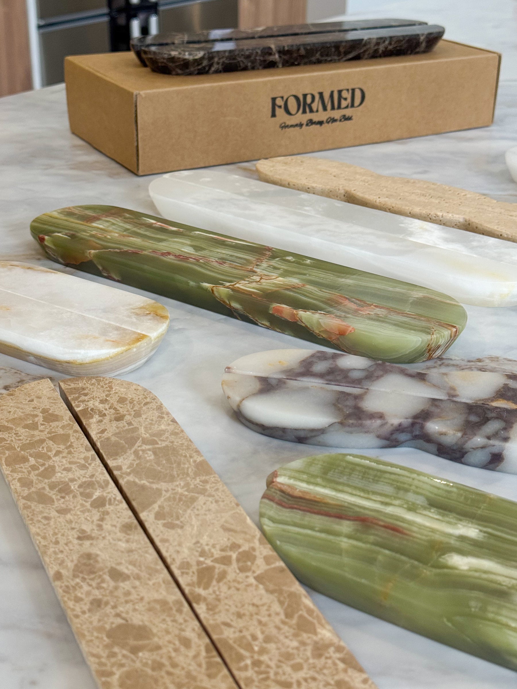 Several polished stone and marble bar tools arranged on a white marble countertop, with a kraft box labeled FORMED in the background.