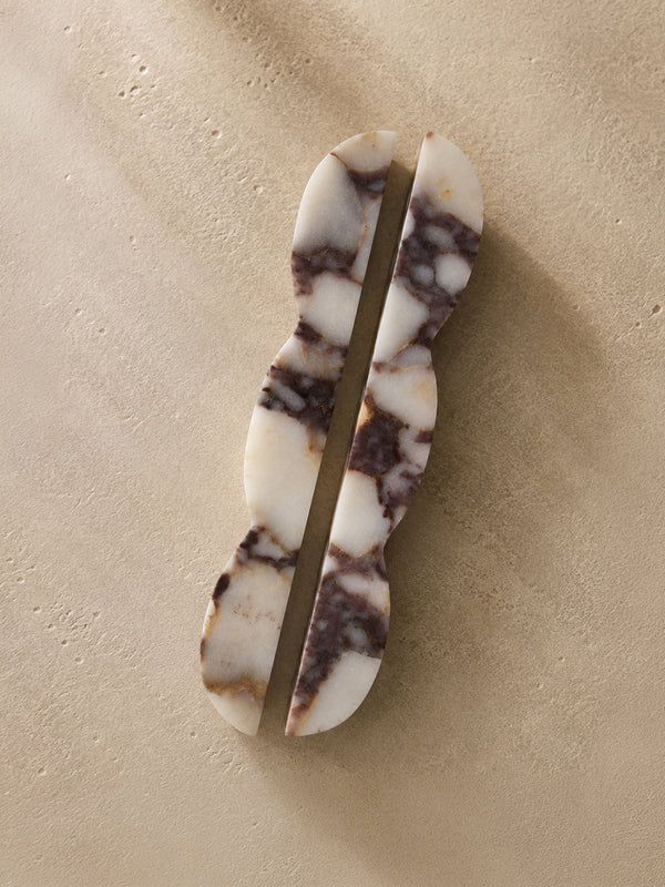 A pair of elongated, wavy hair clips made from white and dark brown marbled stone, displayed on a textured beige background.