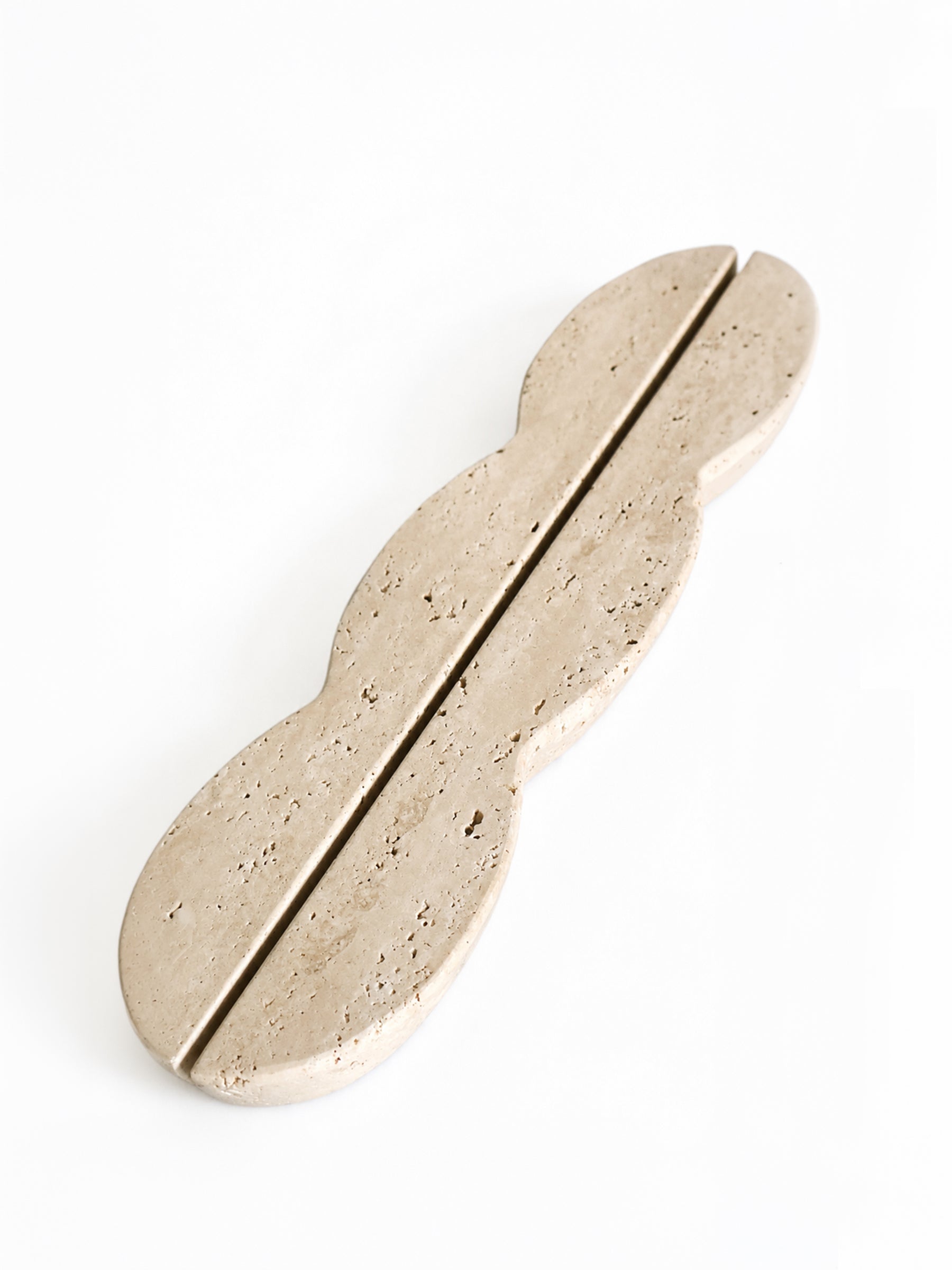 A modern, abstract-shaped door pull handle made of light beige travertine stone, featuring a central split seam and organic wavy contours, shown on a clean white background.