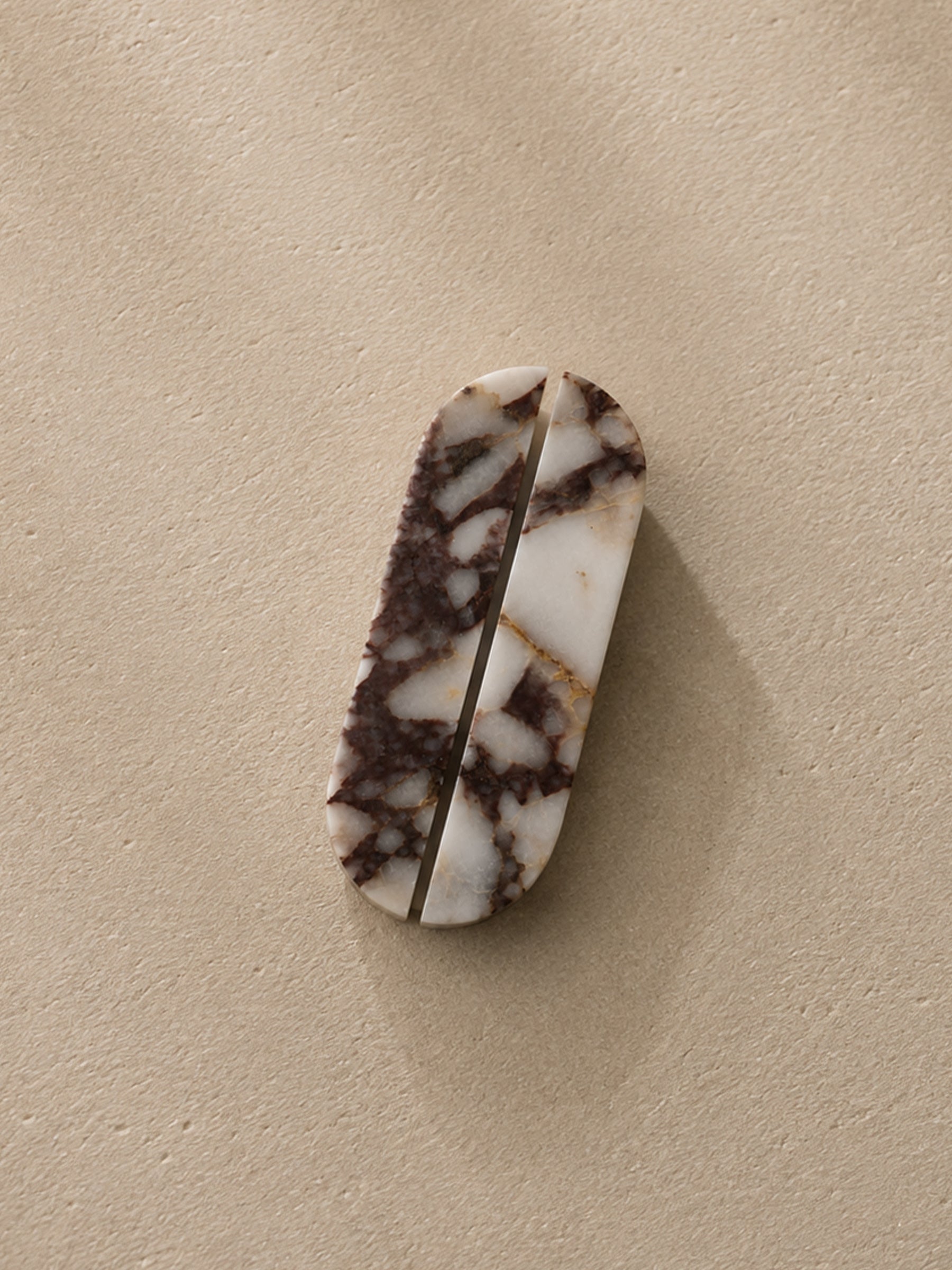 A small oval-shaped carved stone object with a white and dark brown marbled pattern, photographed on a plain beige textured surface.