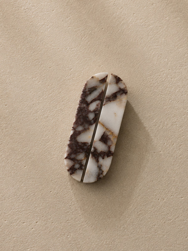 A small oval-shaped carved stone object with a white and dark brown marbled pattern, photographed on a plain beige textured surface.