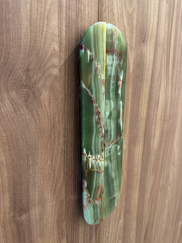 A polished green agate stone wall plaque with natural banding and gold veining, mounted on a brown wood-paneled wall.