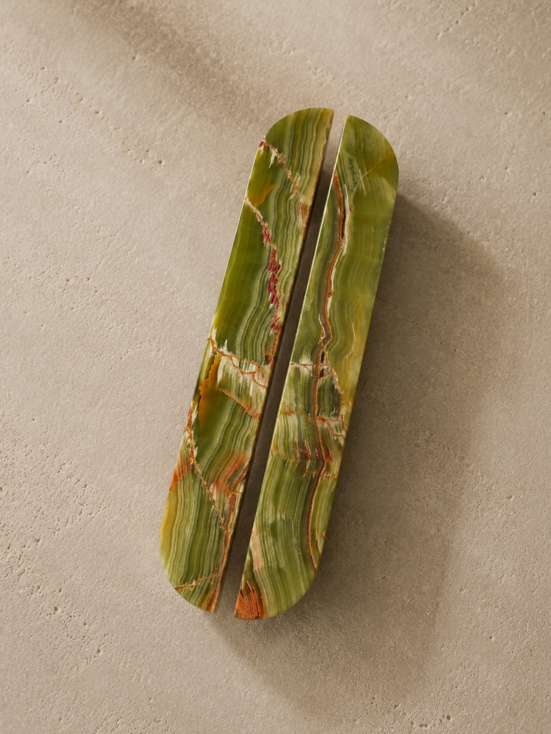 A rectangular wooden box with rounded corners, split vertically down the center, featuring a green and orange striped marble-like wood grain pattern, set against a textured beige background.