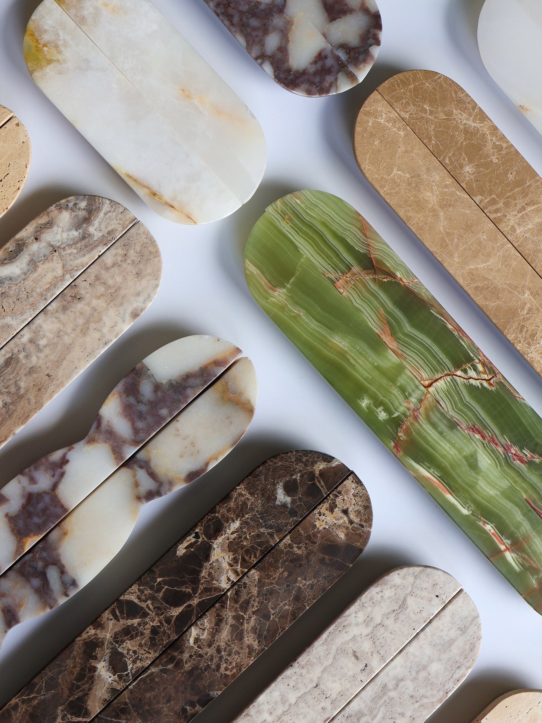 A collection of polished stone slabs in various colors and patterns, including green with red veins, brown, beige, and white, arranged diagonally on a white background.