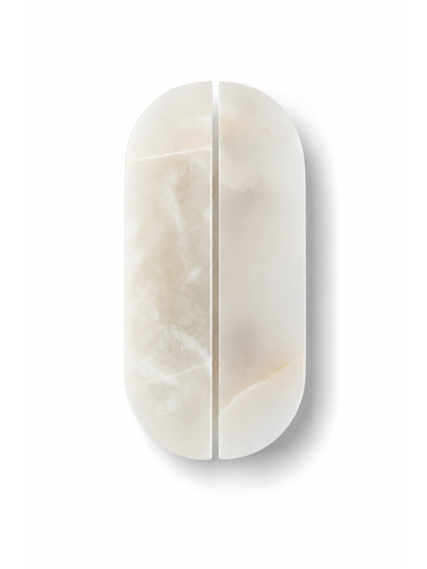 A minimalist, oval-shaped split-screen makeup sponge or applicator made of polished cream-colored marble, shown on a clean white background.