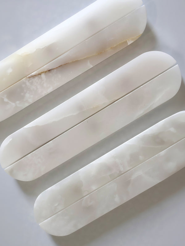 Three elongated cabinet hardware with rounded ends, made from a milky white marbled material, arranged diagonally on a light grey surface.