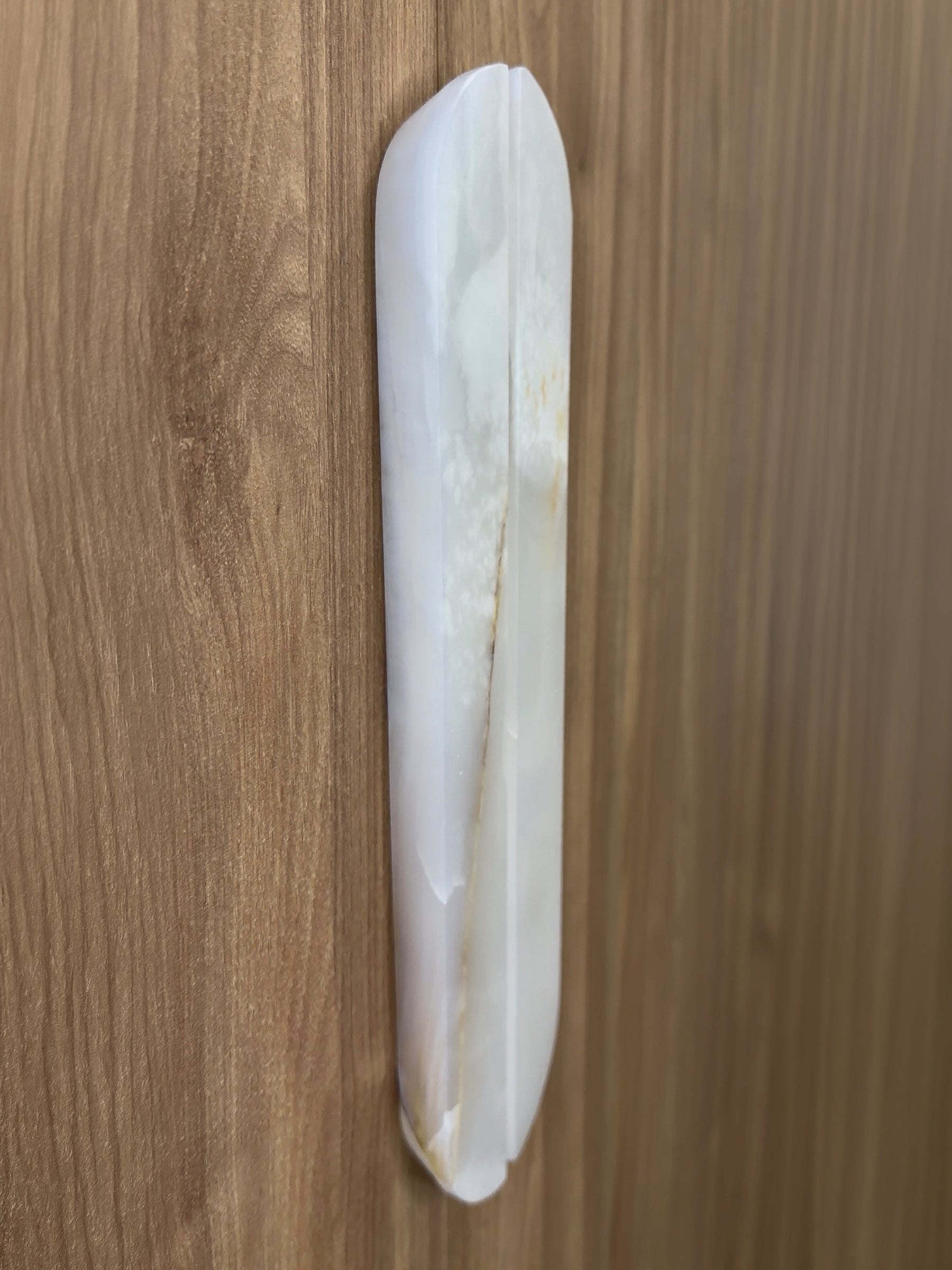 A white oval-shaped wall-mounted door pull handle with a vertical center seam, shown on a brown wood-grain door.