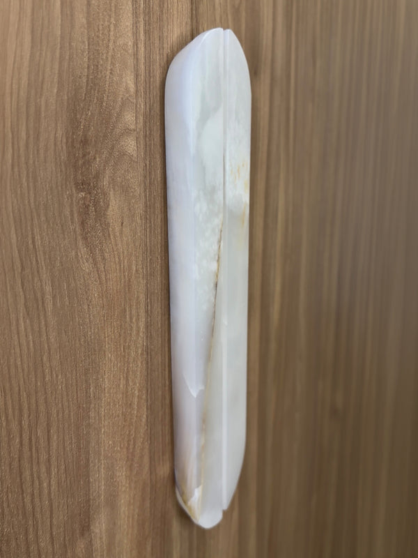 A white oval-shaped wall-mounted door pull handle with a vertical center seam, shown on a brown wood-grain door.