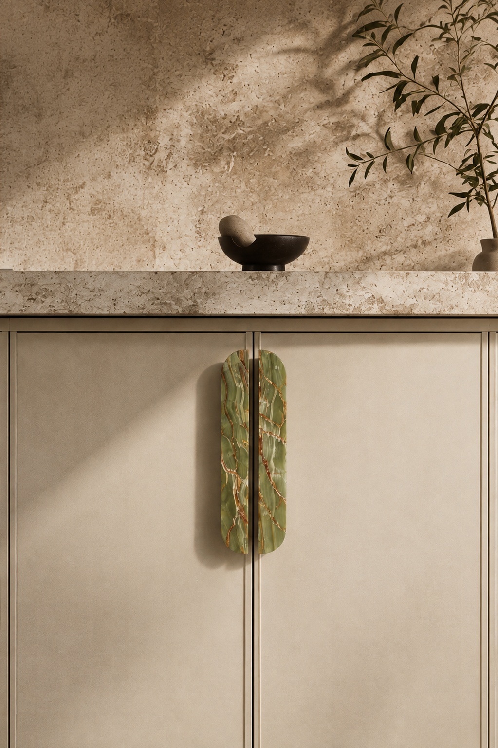 Green and gold marble cabinet handles mounted on a beige cabinet with a stone benchtop and natural styling.