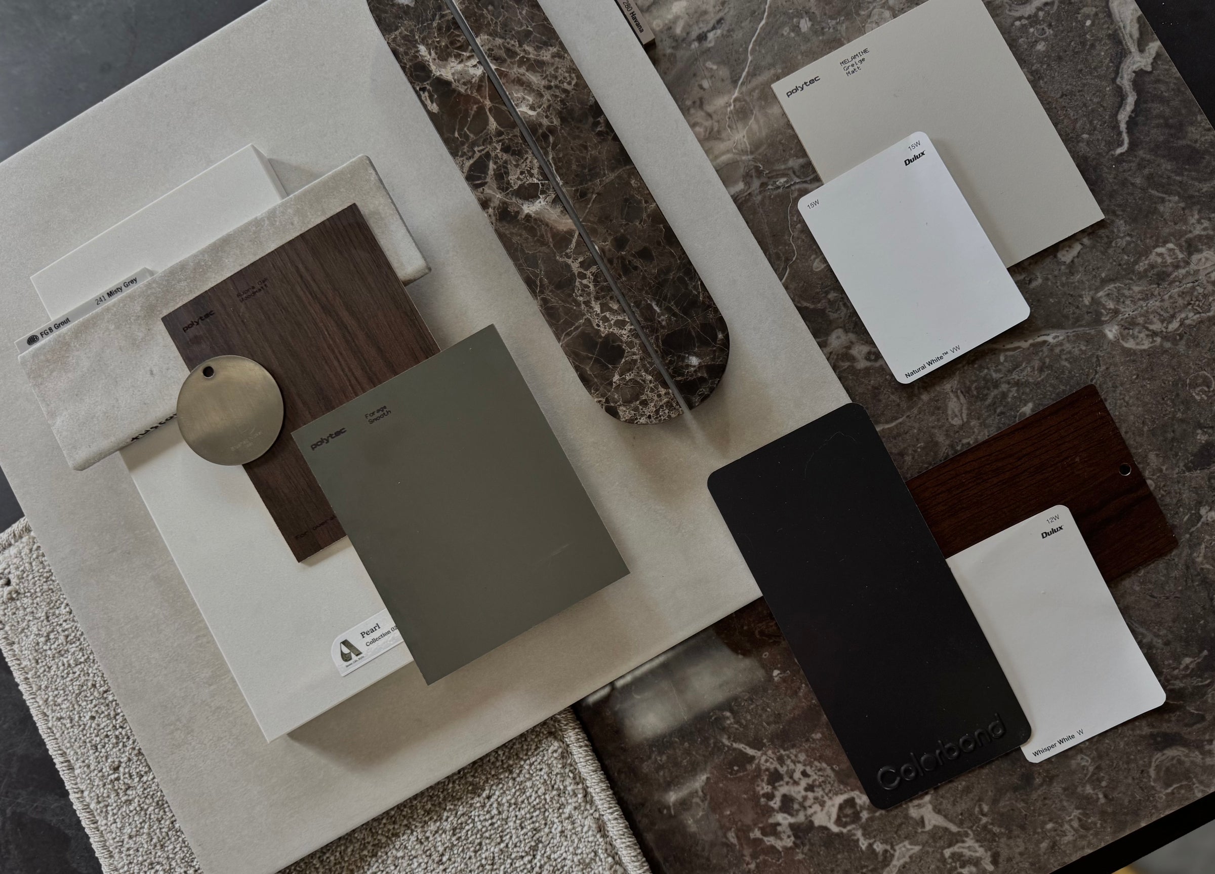 Flat lay of natural stone, timber and material swatches arranged on a dark marble surface for interior design inspiration.