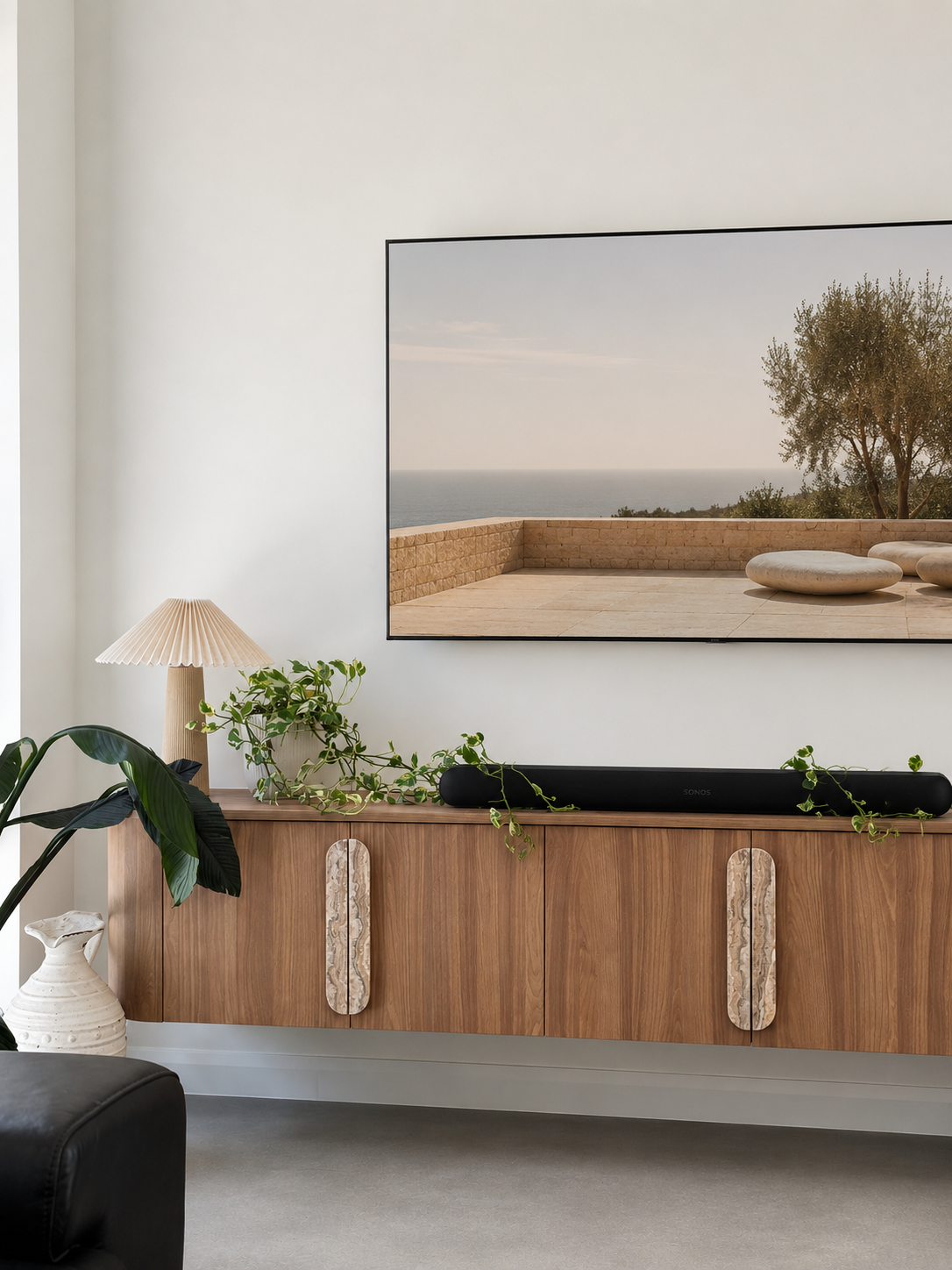 A large framed wall art print depicting a serene beachside terrace scene hangs on a white wall above a wooden media console in a modern living room setting.